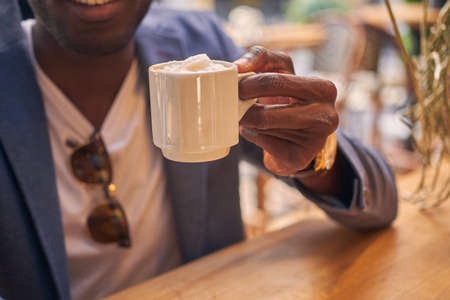 Afro american businessman is enjoying his tasty coffee while sitting at cafe.