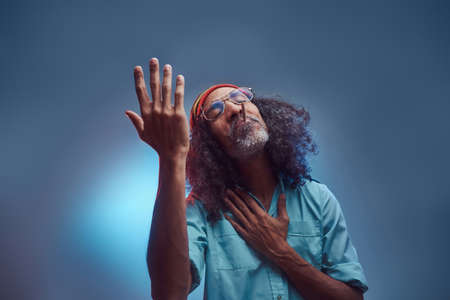 Studio portrait of African Rastafarian male smoking cigarettes. Isolated on a blue background.の写真素材