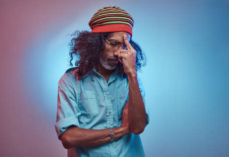 Pensive African Rastafarian male wearing a blue shirt and beanie. Studio portrait on a blue background.の写真素材
