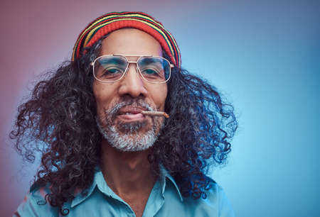 Studio portrait of African Rastafarian male smoking cigarettes. Isolated on a blue background.の写真素材