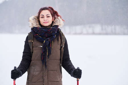 Happy redhead girl doing trekking next to a the snowy forest