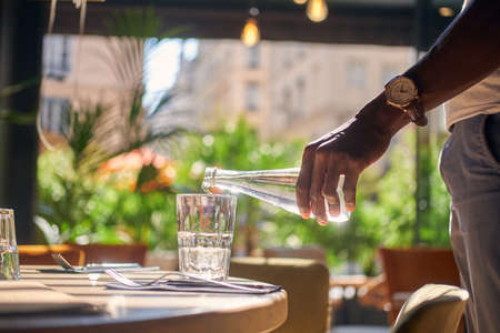 Man with watch on his wrist is pouring fresh water to the glass.