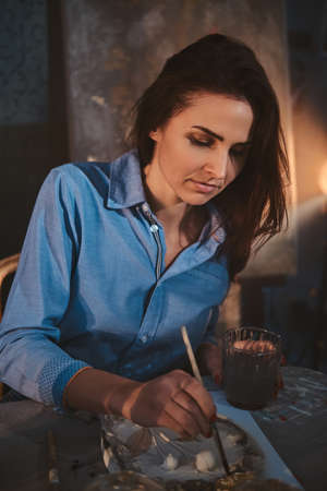 Experienced artist is painting on decorative plate different ornaments.の写真素材