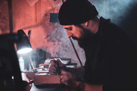 Focused leather designer is working on his new project at workshop.の写真素材