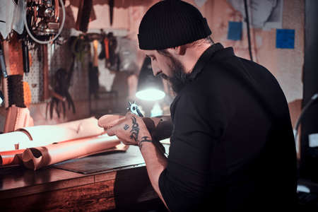 Focused leather designer is working on his new project at workshop.