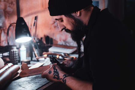 Focused leather designer is working on his new project at workshop.