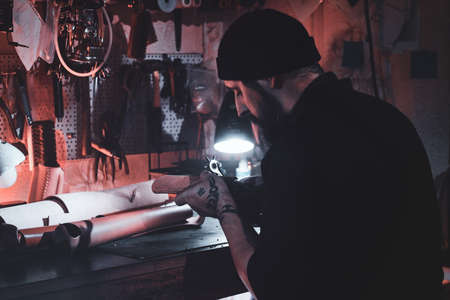 Focused leather designer is working on his new project at workshop.の写真素材