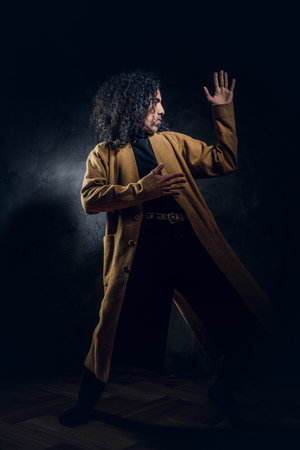 In dark photo studio charismatic styilish man is posing for photographer.
