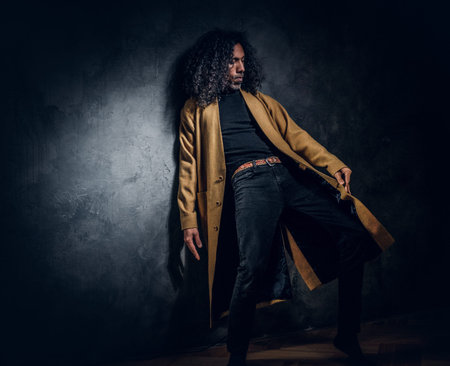 In dark photo studio charismatic styilish man is posing for photographer.