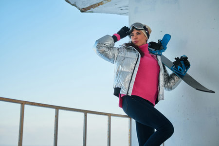 Attractive snowboarder female is posing for photographer with her snowboard.