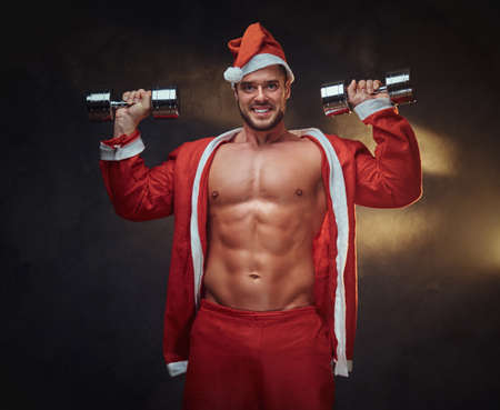 Young attractive man in Santa Claus role is doing exercises with dumbbells.の写真素材