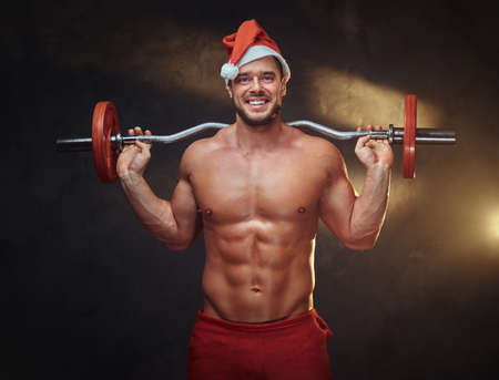 Strong fit man is holding a barbell while posing for photographer in Christmas time.の写真素材