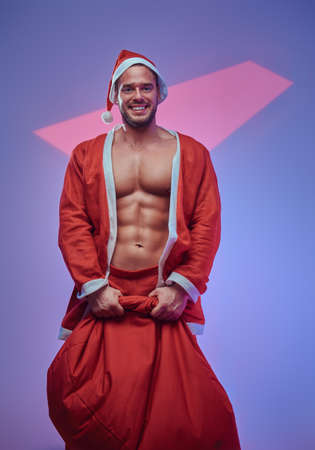 In the light photo studio handsome shirtless guy with bag of gifts is posing for photographer.の写真素材