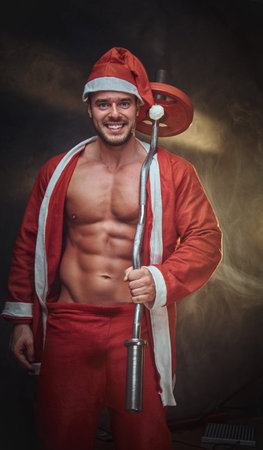 Cheerful handsome man is posing for photographer in Santa costume while holding barbell.の写真素材