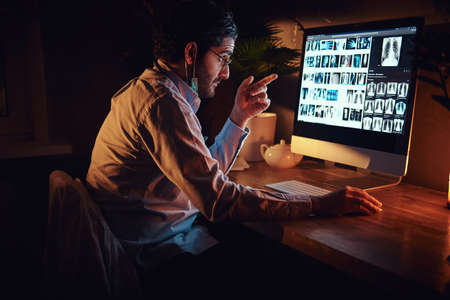 Smart medic in glasses is working with x-ray screens using a computer at dark office.の写真素材