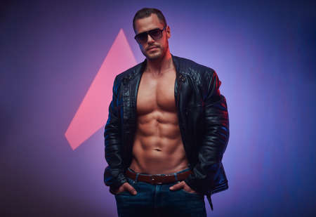 Sexy man in leather jacket and sunglasses is posing for photographer at photo studio.の写真素材