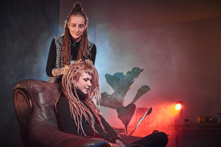 Attractive dreadlock master is working on dreads for pretty blond girl in the dark room.の写真素材