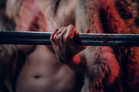 Naked woman with blood stained skin holding a long sword and posing for a camera. Closeup veiw on a hand holding the blade of the sword. Studio photography with red lightの写真素材