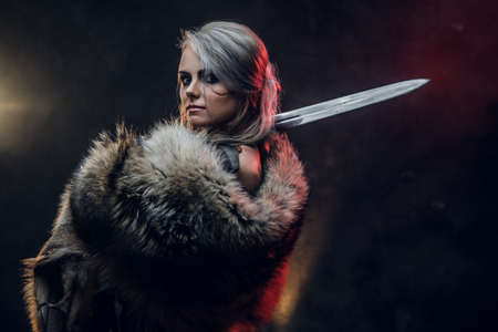 Portrait of a beautiful warrior woman holding a sword wearing steel cuirass and fur. Fantasy fashion. Studio photography on a dark background. Cosplayer as Ciri from The Witcher.の写真素材