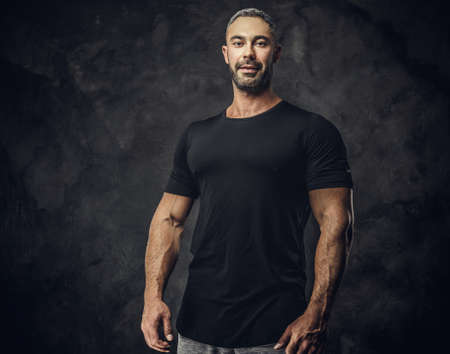 Gorgeous, adult, fit muscular caucasian man coach posing for a photoshoot in a dark studio under the spotlight wearing sportswear, showing his muscles looking calm and kindの写真素材