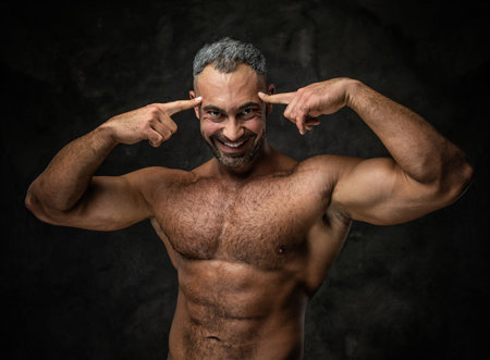 Handsome, adult, fit muscular caucasian man coach posing for a photoshoot in a dark studio under the...
