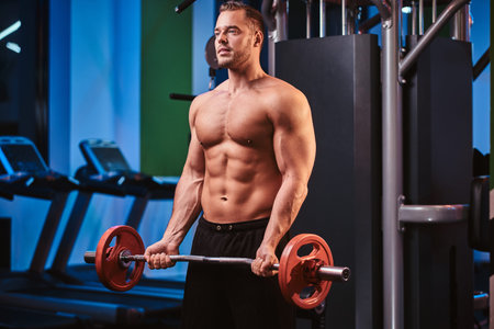 Fit mucular bodybuilder doing weightlifts with barbell in a modern fitness center looking...