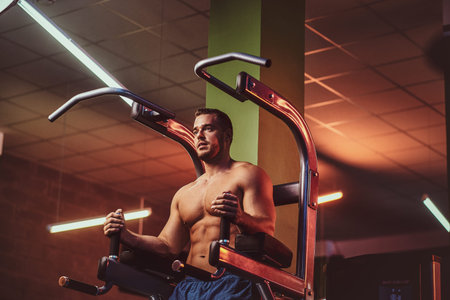 Powerful athletic bodybuilder doing excersise on a parallel bars in a modern fitness center looking relaxedの写真素材