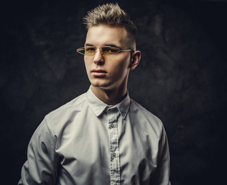 Handsome hipster male model posing in a studio wearing a white shirt, yellow glasses, standing in front of the grey background, looking cool and stylish, close up lookの写真素材