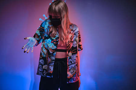 Young woman model looking infected with wuhan coronavirus, stressed out and frightened. Standing in a neon studio, in front of covid-19 projectionの写真素材