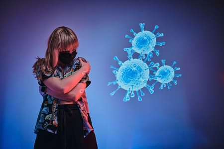 Frightened young woman looking on a coronavirus projection in a neon studio, wearing medical protective mask.の写真素材