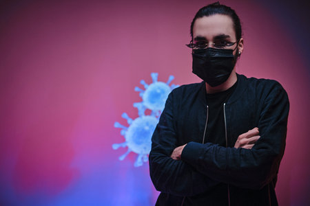 Young caucasian man wearing medical mask, sunglasses and black clothes, standing with hands crossed...