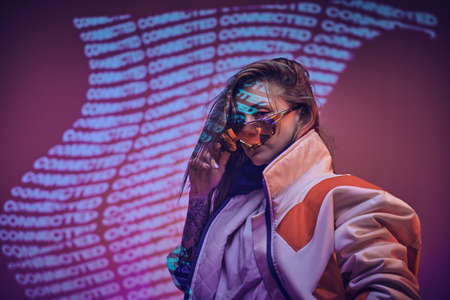 Charismatic young model posing in pink neon studio lights of text projection, wearing vivid racing blazer and holographic sunglasses. Cyberpunk conceptの写真素材