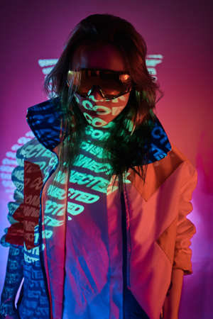Attractive futuristic model wearing holographic glasses and racing blazer, posing in vivid neon studio lights. Cyberpunk conceptの写真素材