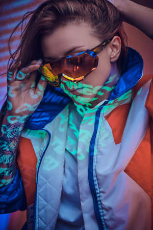 Portrait in close up of a futuristic looking stylish young model, posing in colourful sanglasses in vivid studio lights of text projection, wearing bright red blazer. Cyberpunk conceptの写真素材