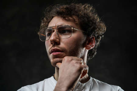 Close-up portrait of a young handsome male model posing on a grey background in a dark studio, wearing white casual shirt and looking seriousの写真素材