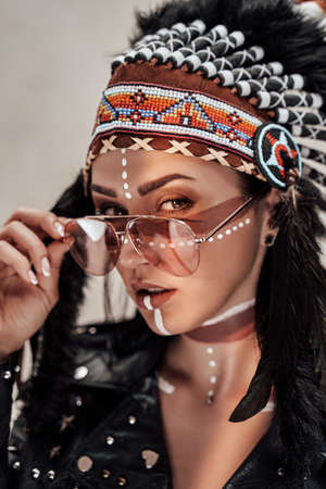 Beautiful and confident female wearing American indian traditional headdress, leather jacket and...