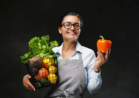 Portrait of a middle-aged female farmer in apron holds a basket of fresh vegetables and fruit....
