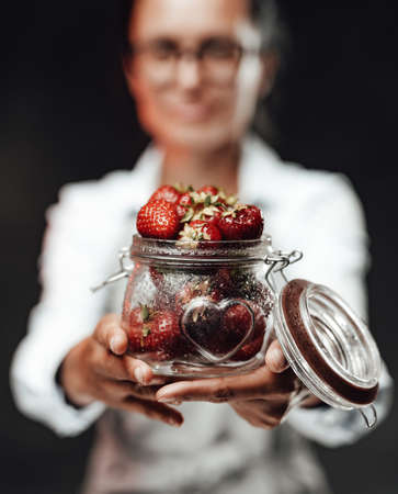Female chef holds a glass with fresh red juicy berries. Close Up view on a wet glass with ripe strawberryの写真素材