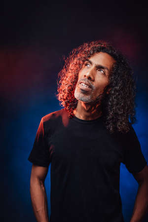 Portrait of a middle aged hispanic male in black t-shirt, lookis pensive. Studio shot on a dark...