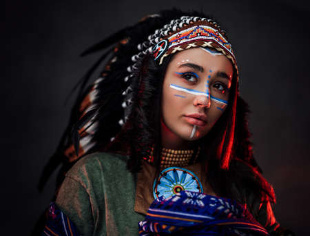 Portrait of a beautiful American Indian woman in ethnical costume and traditional make up. Studio...