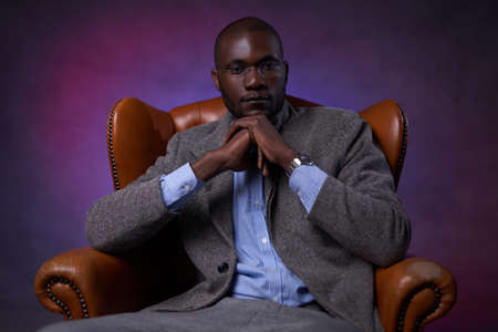 Confident stylish African American businessman sitting on a luxurious leather sofa, looks pensive....