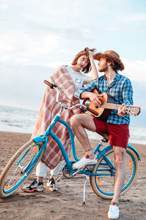 Couple with their bicycle. Boy is playing on the guitar. Girl is wrapped in pink blanket, her arm is on the boys shoulderの写真素材