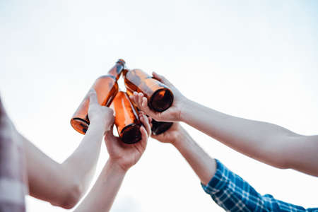 A group of friends, drinking beer on the beach. Hands on the light background