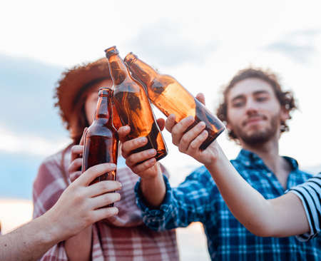 A group of happy friends are spending time relaxing on the beach and drinking beerの写真素材