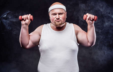 A plump man works out with two small dumbbells. He is wearing a white tracksuitの写真素材