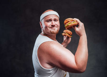 Very corpulent men, with a white bandage on his head, shows his biceps while holding two juicy...