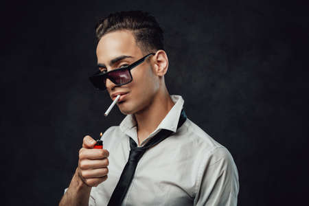 Handsome and successful. Young handsome man in sunglasses wearing white shirt and black tie lights...