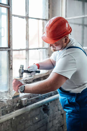 A hardworking builder, with a huge smile on his face, works on a construction site using his hammer...