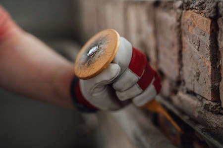 Workers gloved hands with hammer and chisel, getting rid of plaster on a brick wall