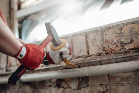 Workers gloved hands with hammer and chisel, getting rid of plaster on a brick wall